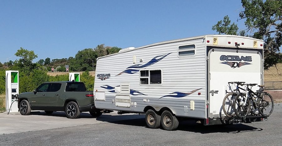 Rivian truck towing travel trailer at charging station