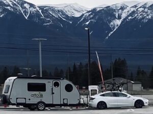 Tesla towing trailer at charging station in front of snow capped mountains