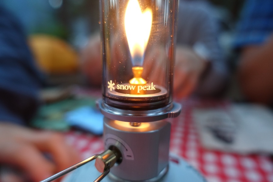 camp lantern on picnic bench with campers blurred in background