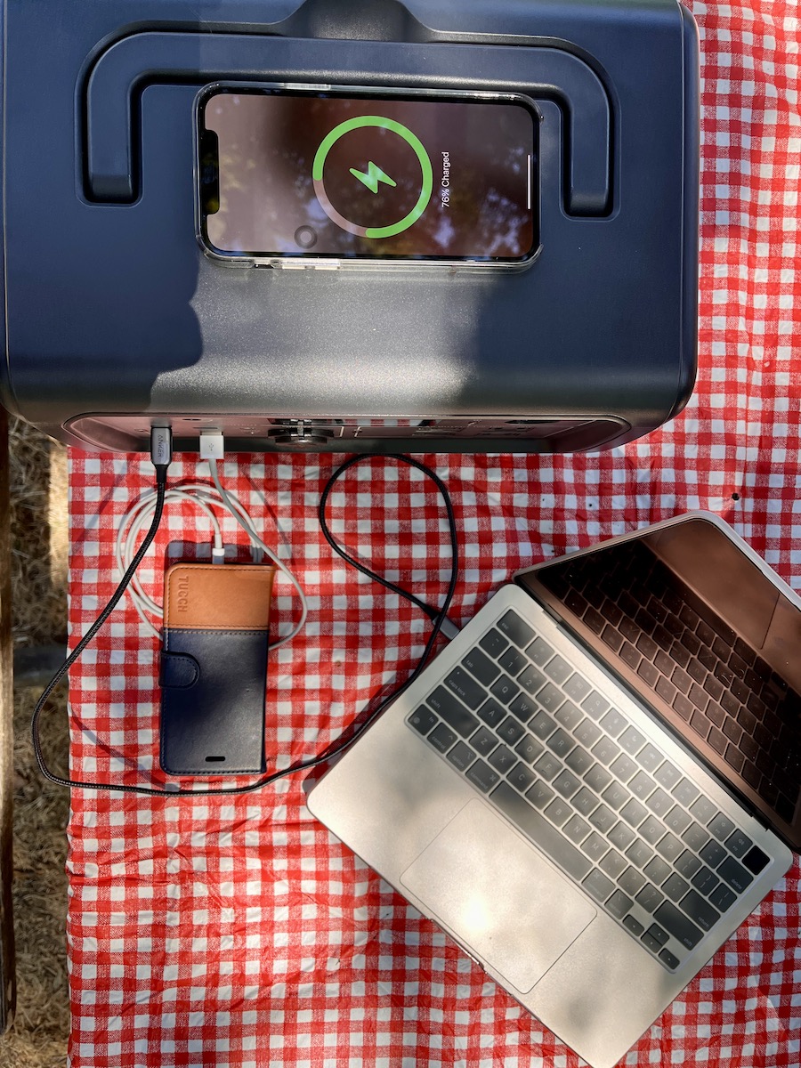 overhead view of Bluetti power station charging two phones and a laptop on checkered picnic table