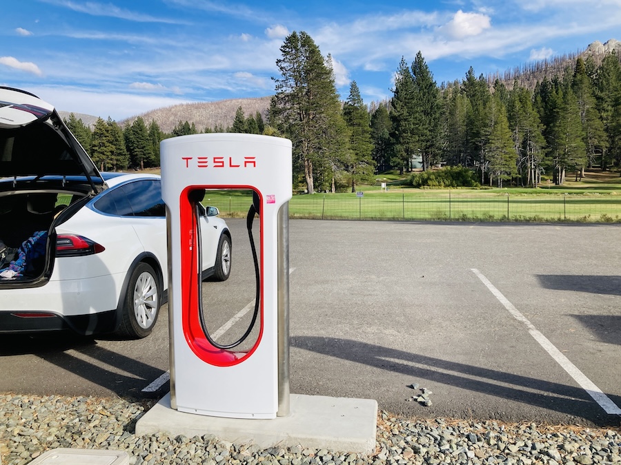 tesla charger, model X with trunk open, and golf course in background